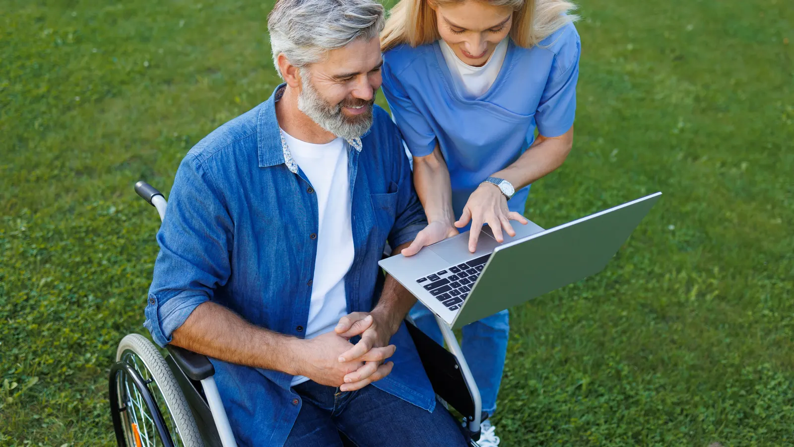 A man in a wheelchair and a support worker looking at a laptop together